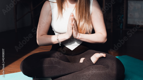 Close-up of young woman in tracksuit midiing indoors. Asana, lotus position, hands folded in prayer. Mindfulness meditation concept, yoga practice, healthy lifestyle