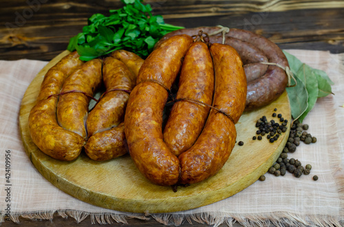 A set of traditional homemade smoked and raw sausages on a round wooden board. Dark wooden rustic background. Copy space