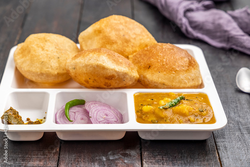 Masala Aloo Sabzi or Indian potato curry served with fried puri or Poori with sliced onion and mango pickle in a white plate  