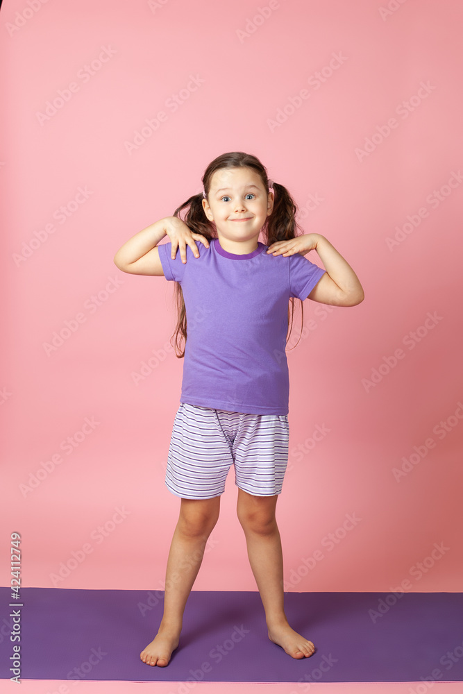 full-length portrait of a smiling girl doing morning exercises and warm-up exercises for the muscles of the shoulders and back, isolated on a pink background. full-length portrait of a smiling girl doing morning exercises and warm-up exercises for the muscles of the shoulders and back, isolated on a pink background.