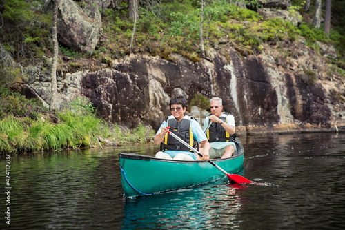 Happy mature couple in life vests canoeing in forest lake. Sunny summer day. Tourists traveling in Finland, having adventure. 