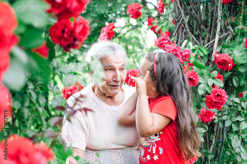 Konstfotografi a gray-haired elderly grandmother plays with her five-year-old granddaughter in the garden under an arch of rose flowers on summer vacation