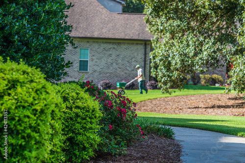 Beautiful landscaping around the front of a house with a landscaper using a spreader to fertilize the lawn in the background photo