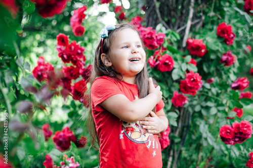 close-up portrait of a laughing, cheerful girl in a red T-shirt under an arch of wild rose or rose hips.