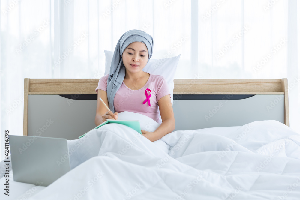 a asian women disease mammary cancer patient with pink ribbon wearing headscarf After treatment to chemotherapy with Take notes in a notebook and laptop on bed In the bedroom at the house,healthcare a asian women disease mammary cancer patient with pink ribbon wearing headscarf After treatment to chemotherapy with Take notes in a notebook and laptop on bed In the bedroom at the house,healthcare