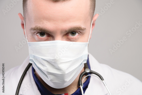 close-up of a male medic face with a serious aggressive look in a medical mask. He looks from under his brows into the camera.