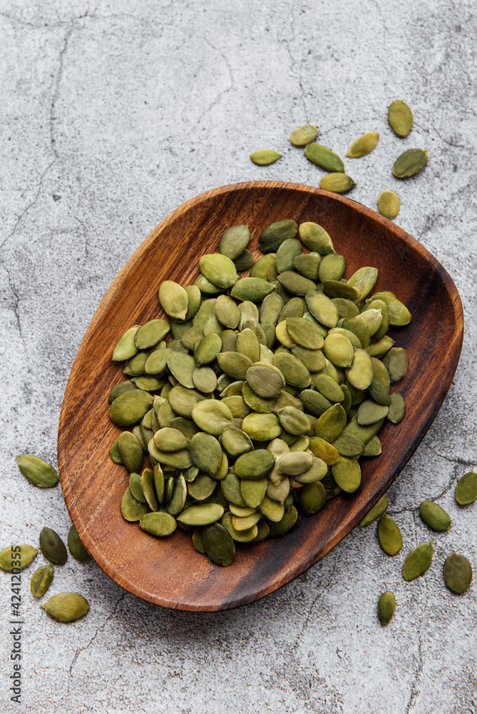 Fototapeta premium Wooden plate with pumpkin seeds on a gray concrete background