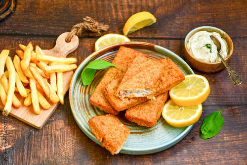 Close up of   crispy breaded  deep fried alaska pollock  fillets  with breadcrumbs served with remoulade sauce french fries  and   fresh lemon