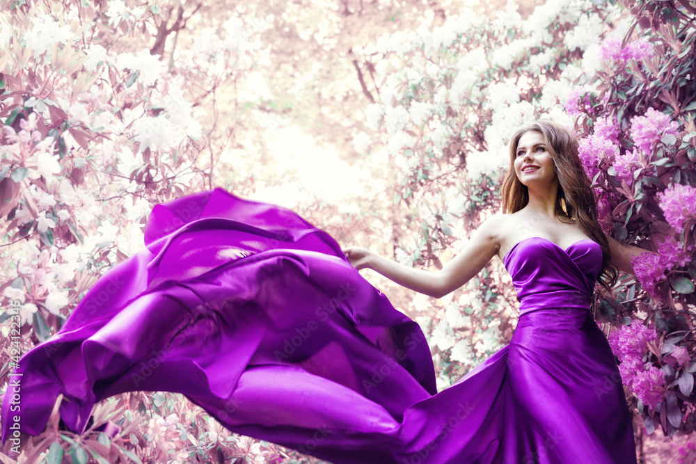 Fototapeta premium Fashion Woman Pink Dress in Spring Flower Garden. Beauty Model Girl in Purple Silk Gown Fluttering on Wind. Floral Pink Fantasy Background