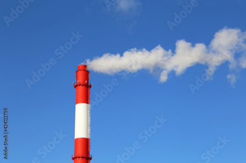 Factory chimney on blue sky background with white smoke. Concept of steam plant, air pollution, heating season