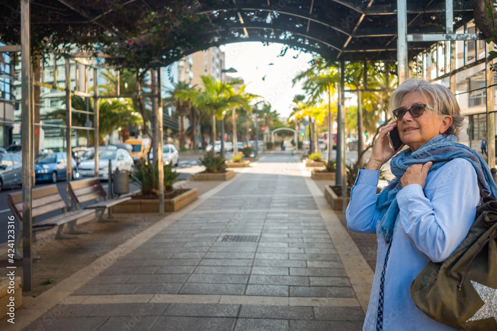 Attractive mature woman standing in the city boulevard while using the mobile phone