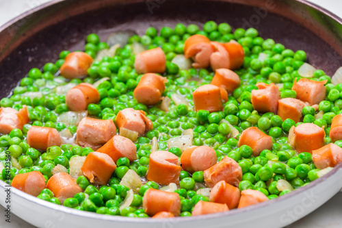 mixture of green peas with sausage in frying pan