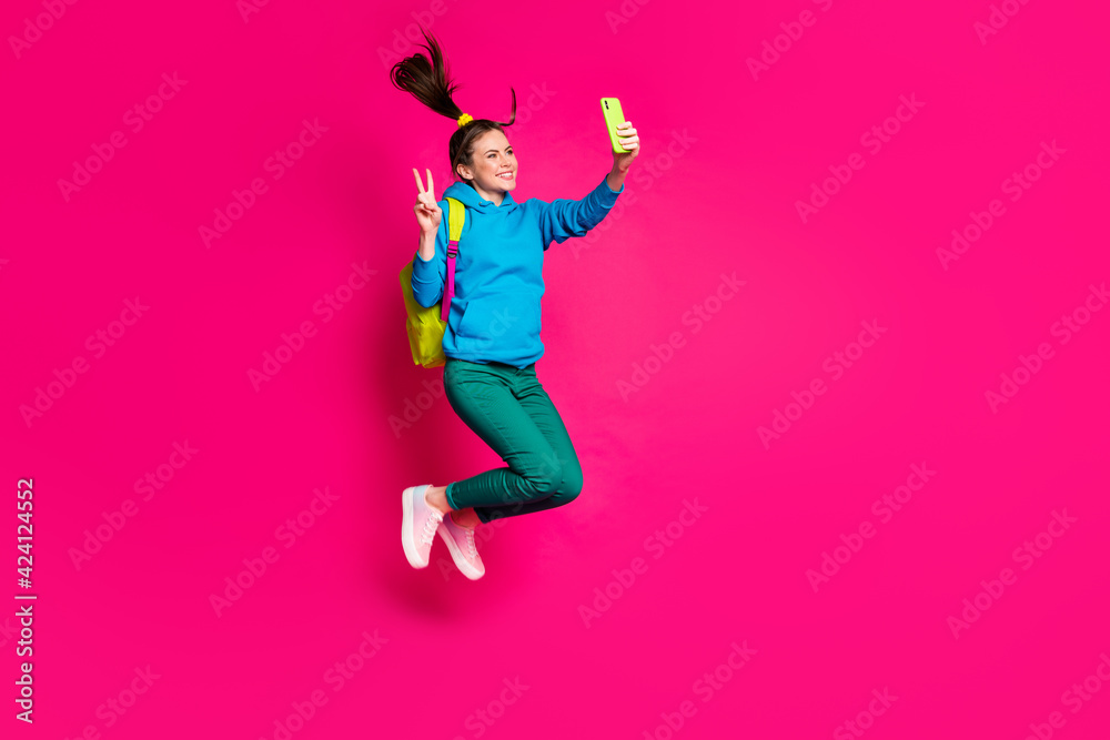 Full length photo of beautiful lady wear blue sweater backpack jumping showing v-sign modern device isolated pink color background