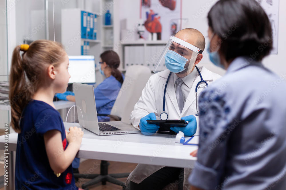 Pediatry specialist talking with little child about healtcare illness in medical clinic. Doctor in treatment disease wearing protective face mask against covid19 during global pandemic Pediatry specialist talking with little child about healtcare illness in medical clinic. Doctor in treatment disease wearing protective face mask against covid19 during global pandemic