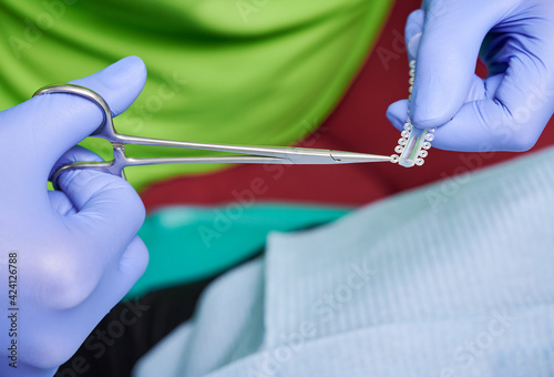 Orthodontist hands cutting elastic ligature ties with dental scissors. photo