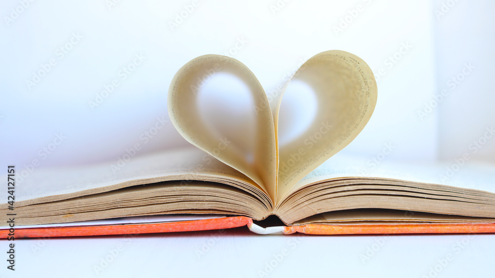 The pages of the book are curved in the shape of a heart with a blurred background. Open book with heart-shaped pages. I love to read. Valentine's day concept. Selective focus. The pages of the book are curved in the shape of a heart with a blurred background. Open book with heart-shaped pages. I love to read. Valentine's day concept. Selective focus.