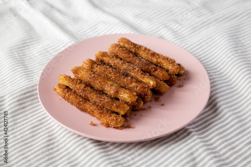 Home-baked Churro Bites on a pink plate on cloth, side view.