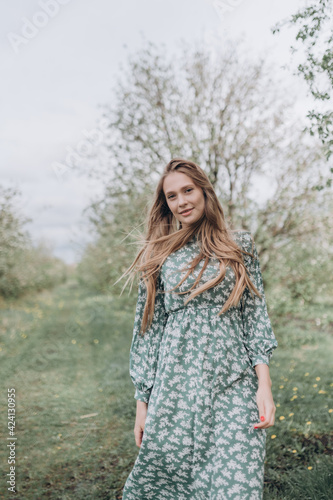 beautiful girl with brown hair in a green dress in a blooming apple orchard with white flowers