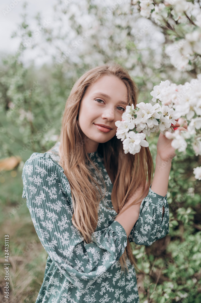 beautiful girl with brown hair in a green dress in a blooming apple orchard with white flowers beautiful girl with brown hair in a green dress in a blooming apple orchard with white flowers