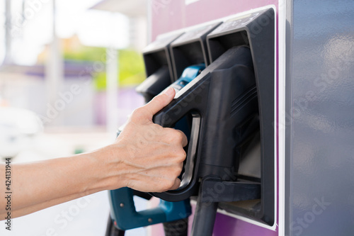 Unrecognizable Asian woman holding aa DC - CCS type 2 EV charging connector at EV charging station.