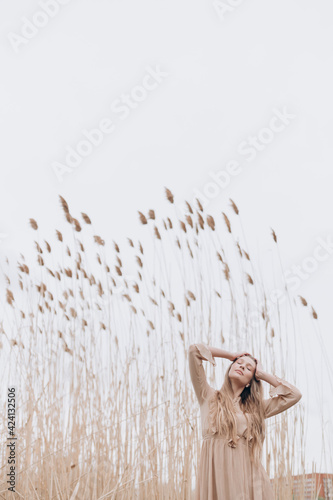a beautiful girl with brown hair in a beige dress stands in the tall reeds by the water © Евгений Александров
