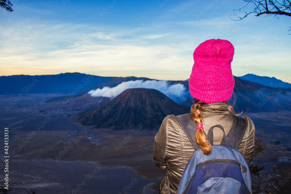 Girl in pink ha is looking at Bromo volcano on sunrise. Mount Bromo is an active volcano in Tengger Semeru National Park, East Java, Indonesia Girl in pink ha is looking at Bromo volcano on sunrise. Mount Bromo is an active volcano in Tengger Semeru National Park, East Java, Indonesia
