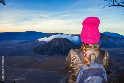 Girl  in pink ha is looking at Bromo volcano on sunrise. Mount Bromo is an active volcano in Tengger Semeru National Park, East Java, Indonesia