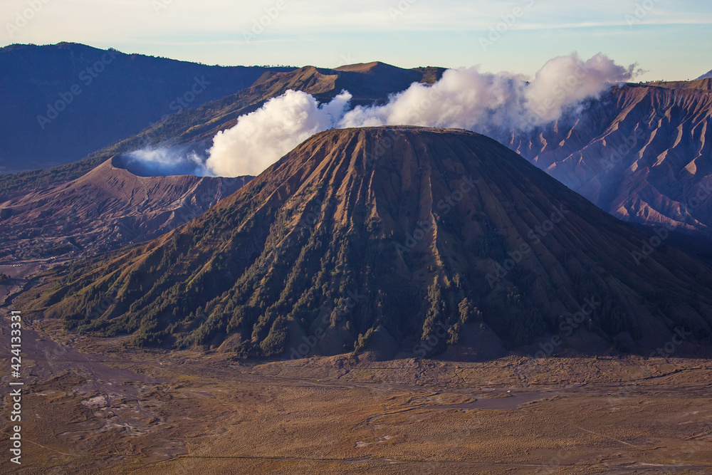 Mount Batok on the foreground and ash of the erupting and active Bromo volcano on the background. Bromo Tengger Semeru National Park, East Java, Indonesia.