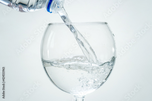 Clear healthy sparkling water is poured from a bottle into a transparent glass on a white background. Closeup