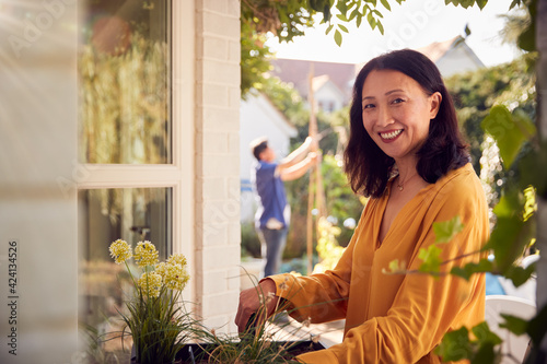 Fotografie Portrait Of Mature Asian Woman Planting Plants Into Wooden Garden Planter At Hom