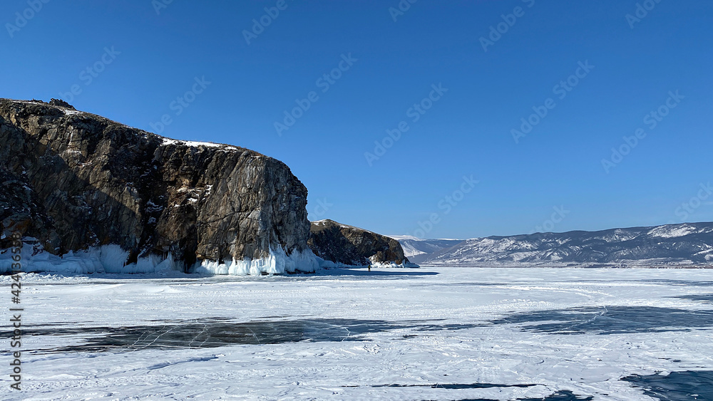 A tourist walks on the ice of frozen Lake Baikal. A beautiful winter landscape with majestic ice-covered rocks