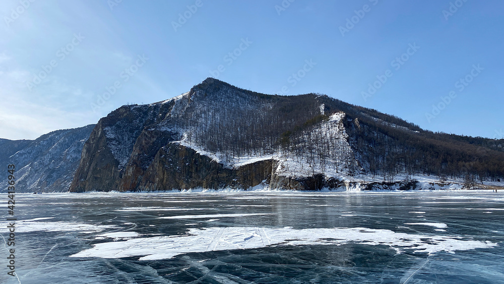 Beautiful panorama of frozen Lake Baikal. Stone, forested rocks, mountains and hills of Olkhon Island.