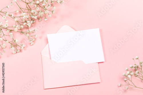 Pastel pink festive layout with envelope, empty sheet, white gypsophila flowers. Copy space for text. Mock up.