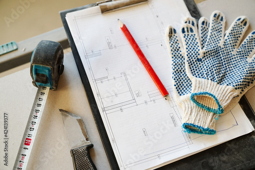 Working process. Knife, tape measure, blueprint, pencil and gloves lying on the drywall sheet