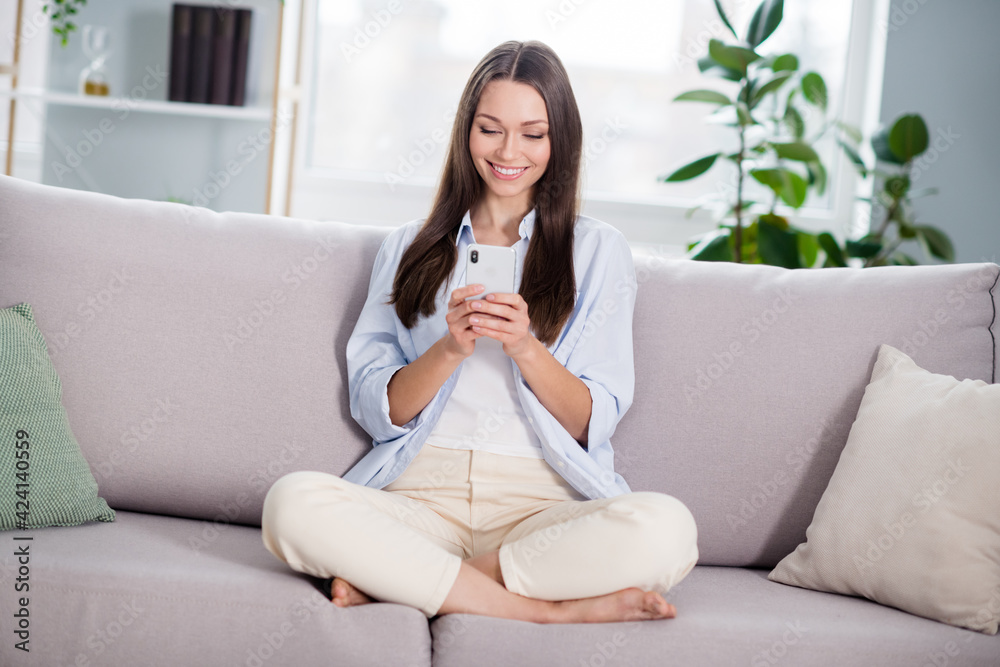 Full size photo of nice optimistic brunette long hairdo lady sit on coach look telephone wear blue shirt at home Full size photo of nice optimistic brunette long hairdo lady sit on coach look telephone wear blue shirt at home