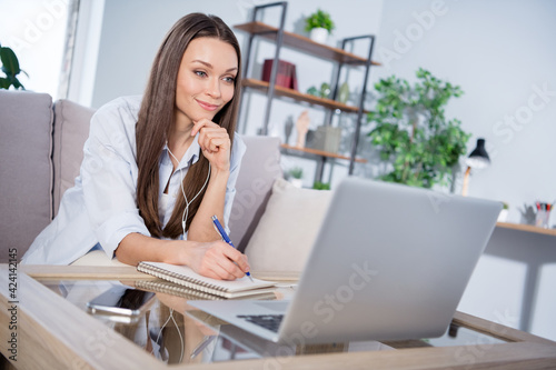 Photo of nice optimistic brunette lady sit with headphones write talk laptop wear shirt alone at home