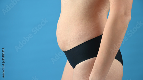 Midsection of pregnant woman by blue background with copy space  start of pregnancy.