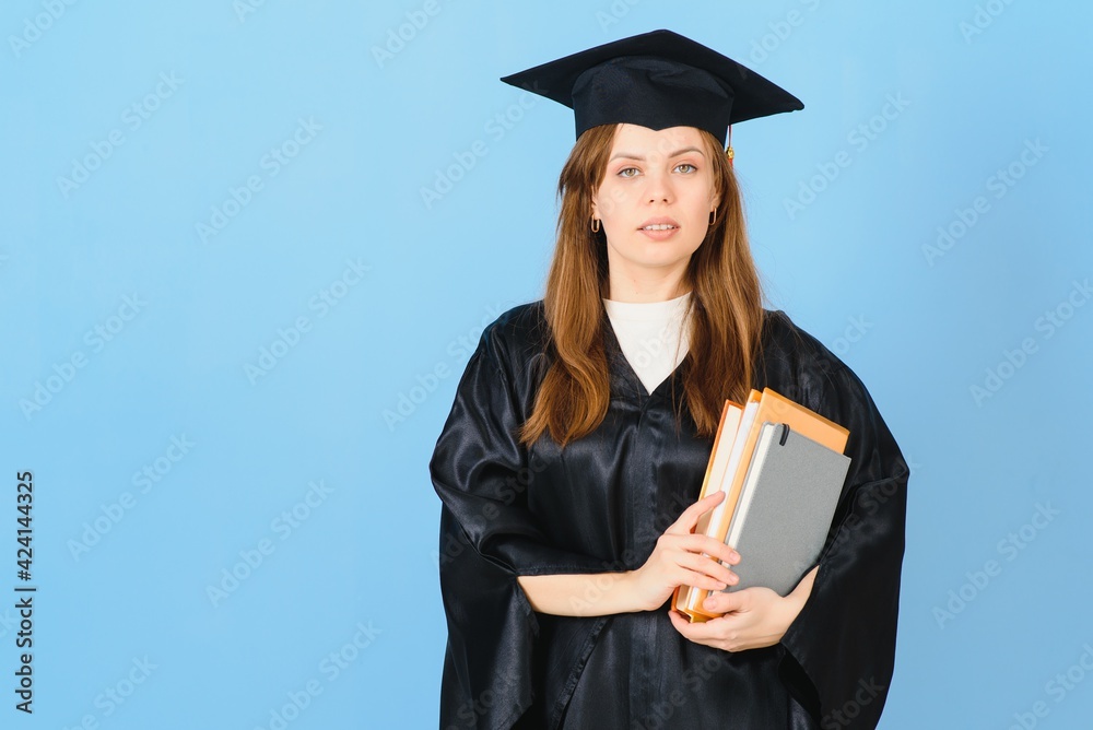 Woman graduate student wearing graduation hat and gown, on blue background Woman graduate student wearing graduation hat and gown, on blue background