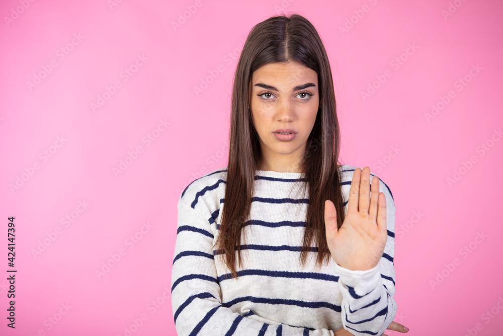 Woman making stop gesture with her hand. Prohibition symbol. Closeup portrait of young, serious, pretty, charming girl in sweater making stop gesture with palm of her hand on pink background Woman making stop gesture with her hand. Prohibition symbol. Closeup portrait of young, serious, pretty, charming girl in sweater making stop gesture with palm of her hand on pink background