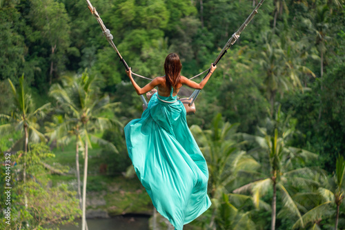 Woman in long turquoise dress swinging in the jungle, Bali