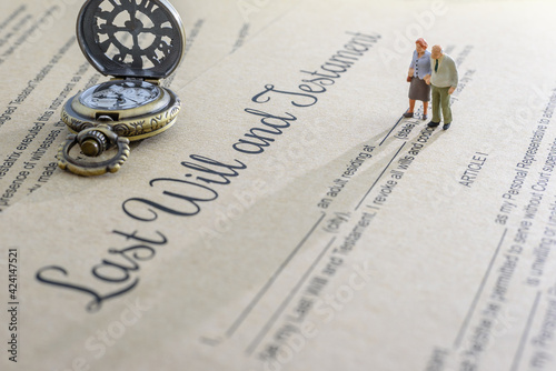 Last will and testament / legacy, inheritance or death tax concept : Miniature elder / old couple stands on a legal document form, depicts preparing to transfer properties to their heirs after death photo
