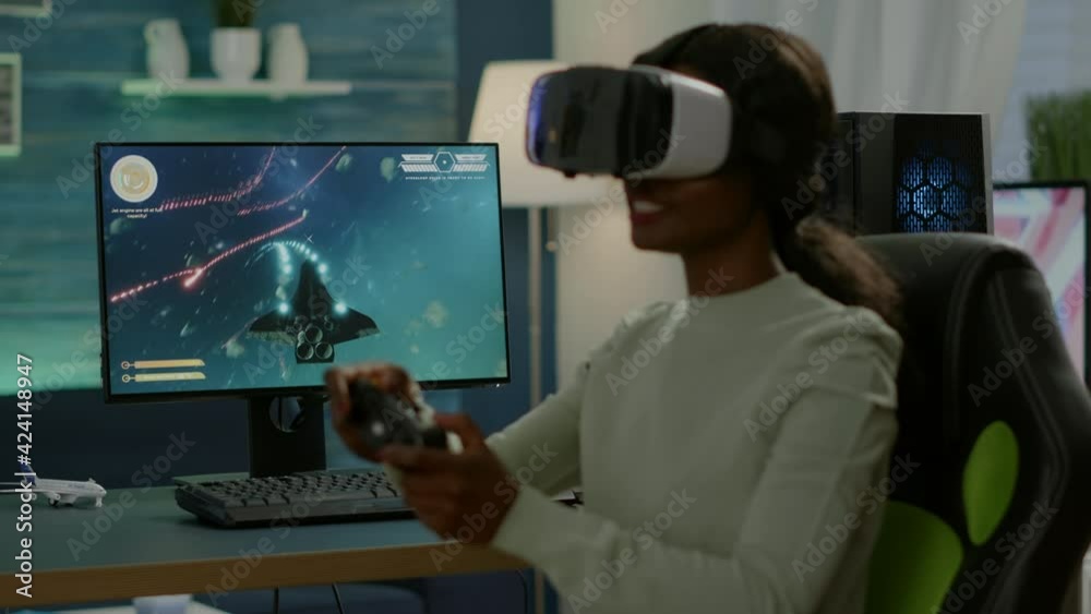 African gamer playing space shooter competition using virtual reality goggles. Competitive player using joystick for online championship sitting on gamining chair late at night in living room African gamer playing space shooter competition using virtual reality goggles. Competitive player using joystick for online championship sitting on gamining chair late at night in living room
