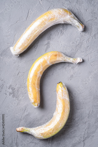 Banana fruits wrapped in stretch plastic on grey background