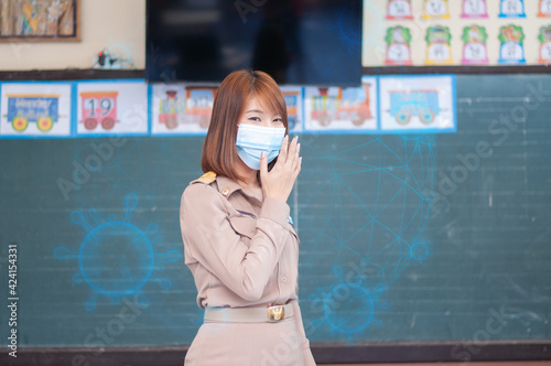 Female thai teacher in uniform standing in front of the classroom wearing mask with blue virus around her
