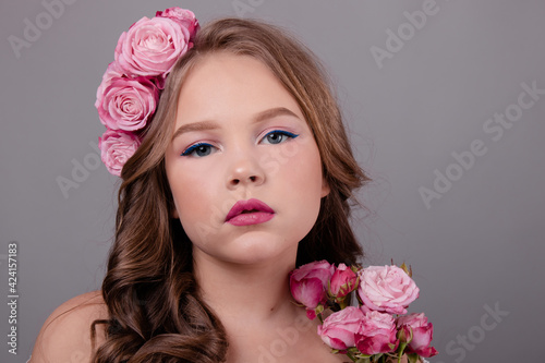 brunette teenage girl with pink roses in her hair on gray background. flowers in curls on the head. fashion photo © OliaVesna