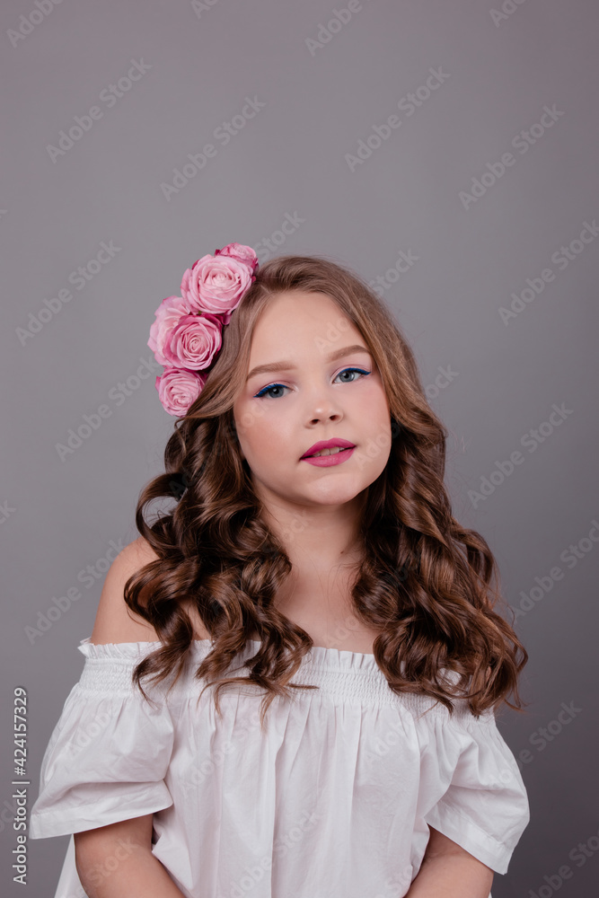 brunette teenage girl with pink roses in her hair on gray background. flowers in curls on the head. fashion photo