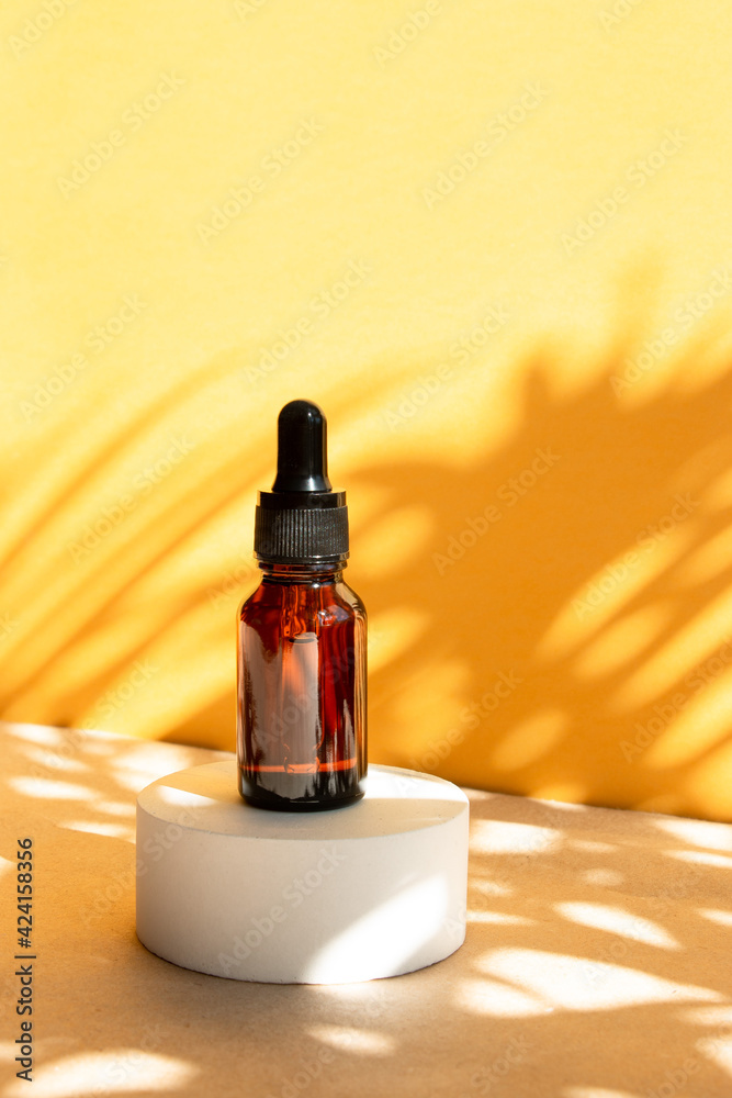 A cosmetic bottle with an amber glass dropper sits on a concrete pedestal. Natural beauty products. Mineral organic oil. Empty bottle for skin care. Hard sunlight. A cosmetic bottle with an amber glass dropper sits on a concrete pedestal. Natural beauty products. Mineral organic oil. Empty bottle for skin care. Hard sunlight.