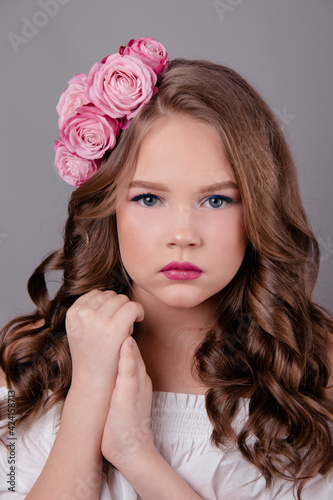 portrait of pretty brunette girl with pink roses in her hair on gray background. flowers in curls on the head. spring, flowering, colors. fashion photo
