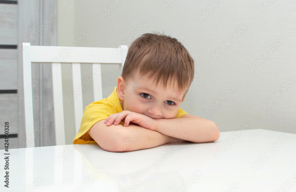 A frustrated, sad, tired, disappointed boy sits at a white desk. A frustrated, sad, tired, disappointed boy sits at a white desk.