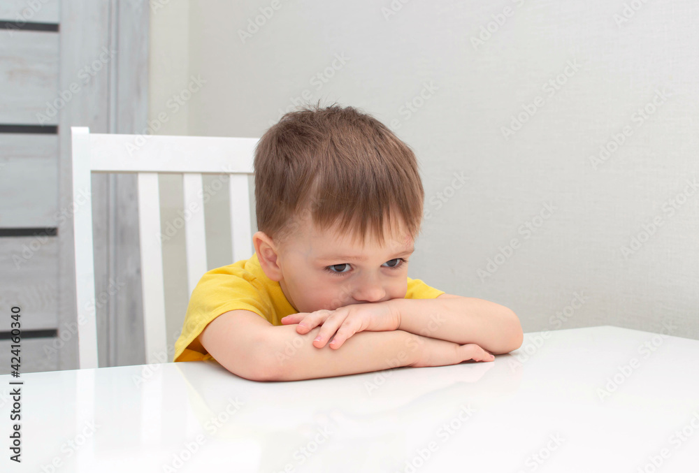A frustrated, sad, tired, disappointed boy sits at a white desk. A frustrated, sad, tired, disappointed boy sits at a white desk.